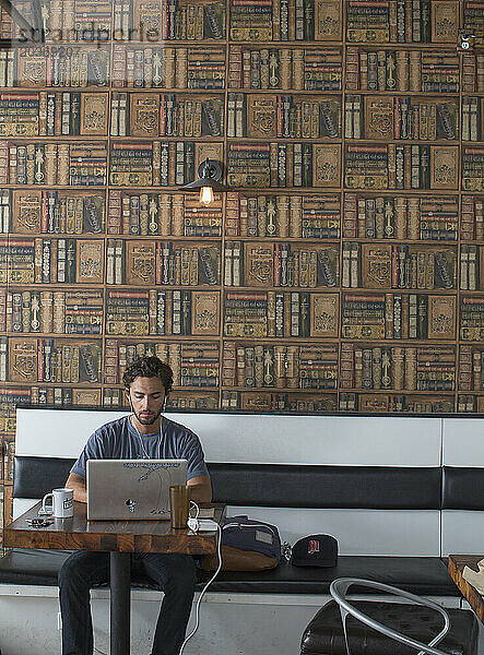 Ein Mann sitzt in einem Café und arbeitet an seinem Laptop.