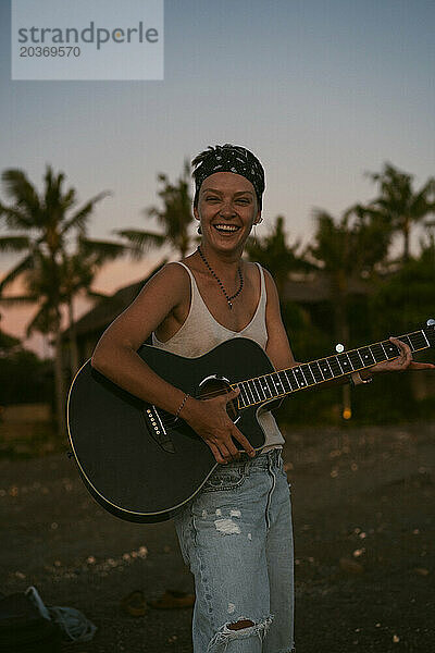 Musikerin singt und spielt Gitarre am Strand. In einem Bandana. Bali