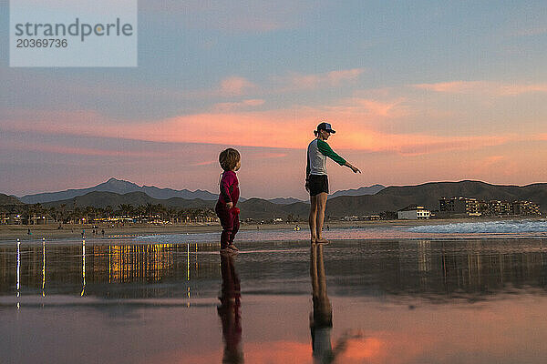 Eine Mutter und ihr Sohn gehen bei Sonnenuntergang am Strand spazieren.