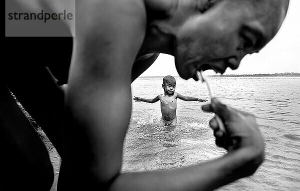 Mutter putzt Zähne  während Sohn spielt  am Red River  Vietnam.