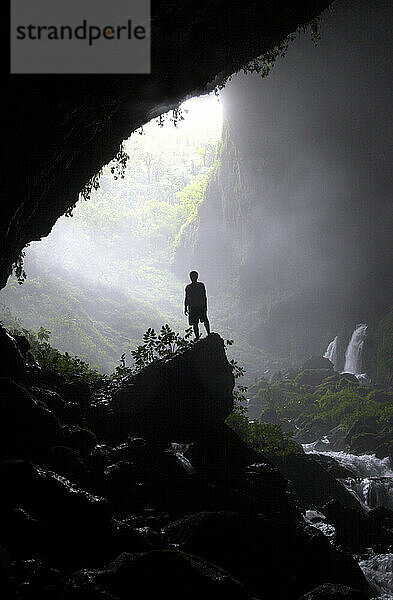 Ein Stammesangehöriger steht auf einem Felsen am Eingang einer riesigen Flusshöhle in New Britain