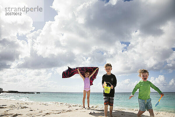 Drei glückliche Geschwister spielen zusammen am wolkigen Karibikstrand