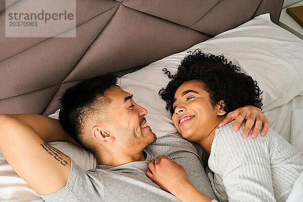 Multiethnisches glückliches Paar  das sich im Bett liebevoll anschaut.