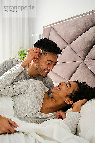 Vielfältiges romantisches Paar wacht während der Flitterwochen gemeinsam im Bett auf.