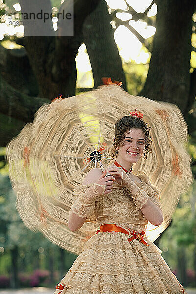 Eine junge Frau posiert in einem Southern Belle-Outfit  einschließlich eines großen  verzierten historischen Kleides und eines Sonnenschirms  unter einem Baum.