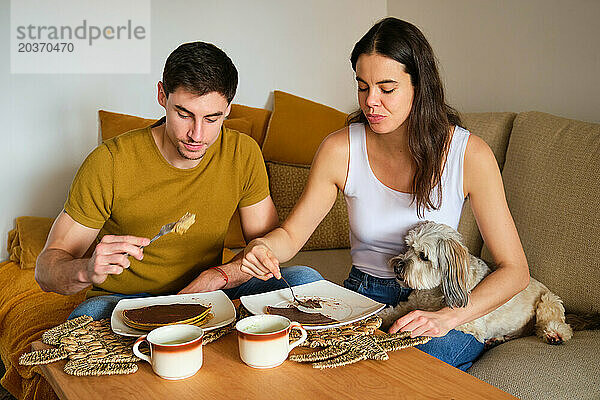 Spanisches Paar isst zu Hause Pfannkuchen mit seinem Hund.