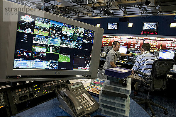 Zwei Männer arbeiten in einem Raum voller Fernsehbildschirme und Computermonitore im Kontrollraum von ESPN in Bristol  Connecticut.