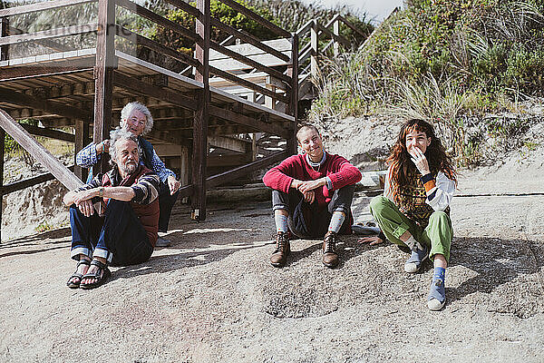 Eine Generation von Familien sitzt lächelnd zusammen auf einem Felsbrocken am Meer