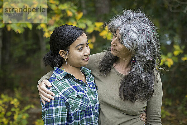 Eine weiße Mutter legt einen Arm um ihre gemischtrassige Teenager-Tochter