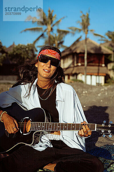 Musikerin singt und spielt Gitarre am Strand. In einem Bandana. Bali