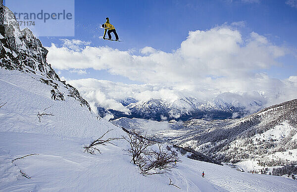 Ein Mann springt an einem sonnigen Tag am Cerro Catedral in Argentinien auf seinem Snowboard von einer Klippe