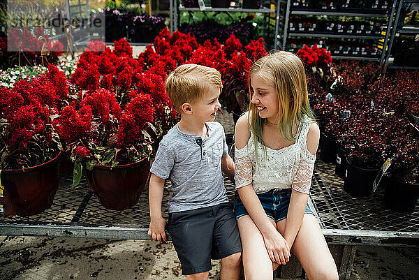 Teenager-Mädchen und kleiner Junge lächeln einander umgeben von Blumen an.