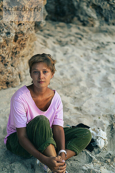 Frau mit kurzen Haaren entspannt am Strand von Bali und beobachtet den Sonnenuntergang.