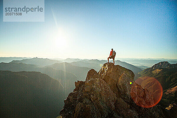 Erfolgreicher Wanderer mit Rucksack steht auf Berggipfel  Sonnenuntergang