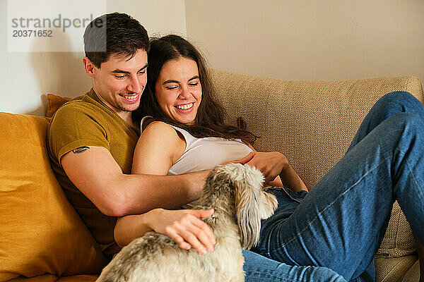 Spanisch lächelndes verliebtes Paar auf dem Sofa mit seinem Hund.