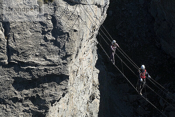 Zwei Personen laufen über den engen Kabelbrückenabschnitt eines Klettersteigs in den französischen Alpen.