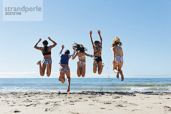 Mädchen springen gemeinsam am Strand.