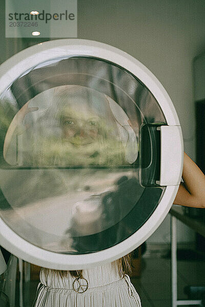 Eine junge Frau wäscht in einer öffentlichen Wäscherei Wäsche und hat Spaß.