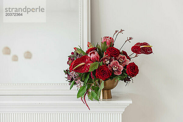 Lebendiges Blumenarrangement in großen Rottönen in einer goldenen Vase