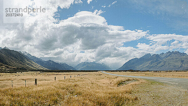 Eine Landstraße schlängelt sich durch Weideland und Berge in der Landschaft Neuseelands