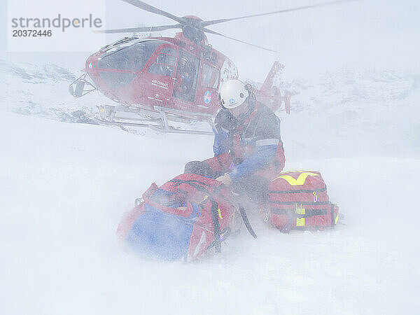 Rettungskräfte helfen einem verletzten Skifahrer im Skigebiet Zermatt in den Schweizer Alpen. Der Notarzt schützt sich und den Patienten vor dem Abwind der Landung