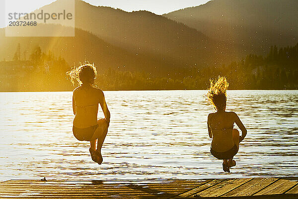Zwei glückliche junge Frauen springen bei Sonnenuntergang in Idaho in einen See.