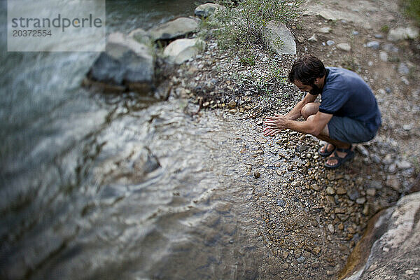 Ein Mann kauert und wäscht sich in einem Fluss in Joes Valley  Utah  die Hände.