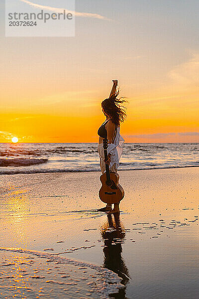 Musikerin mit Gitarre am Strand bei Sonnenuntergang. Bali