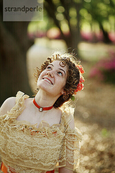 Eine junge Frau posiert in einem Southern Belle-Outfit  einschließlich eines großen  verzierten historischen Kleides und eines Sonnenschirms  unter einem Baum.