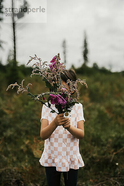 Junges Mädchen hält lila Blumen im Feld