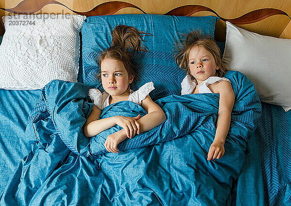 Zwei kleine lächelnde süße Schwestern liegen im Bett  Draufsicht.
