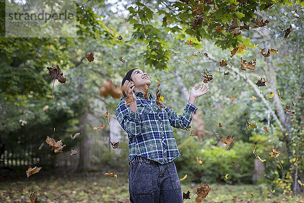 Biracial teen girl throwing up fall leaves and laughing