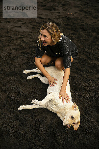 Mädchen streichelt einen Labrador Retriever im Sand am Strand