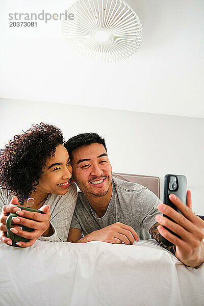 Multiethnisches glückliches Paar macht ein Selfie im Bett.