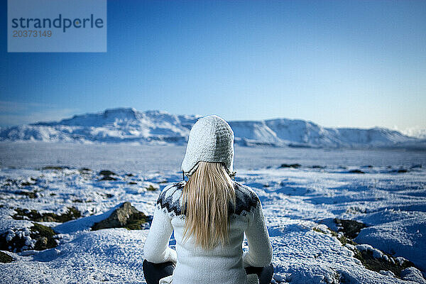 Eine Frau in einem Wollpullover sitzt in einer Winterlandschaft