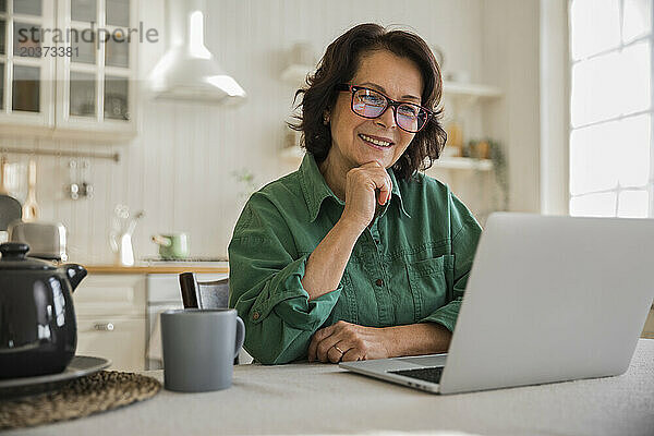 Eine ältere  fröhliche Frau mit Brille schaut lächelnd auf den Laptop-Bildschirm
