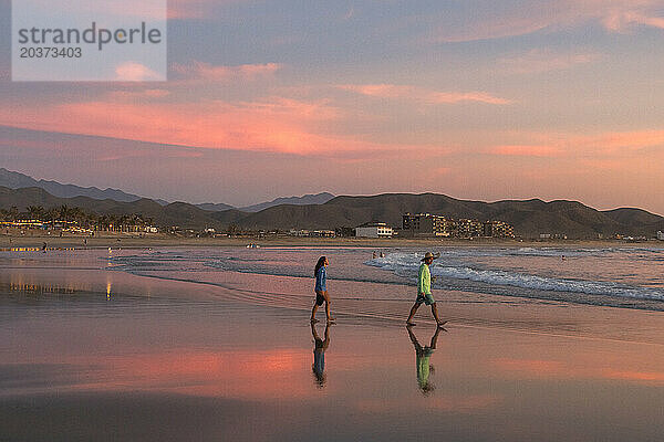 Zwei Menschen gehen bei Sonnenuntergang den Strand entlang.