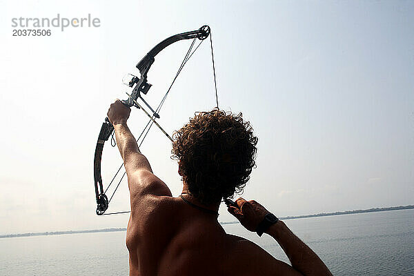 Silhouette eines jungen Mannes beim Bogenschießen auf dem offenen Wasser.