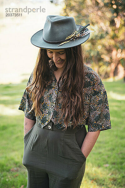 Frau lächelt mit Hut  Federn und Blumenhemd draußen