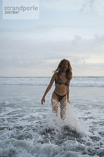 Porträt einer fröhlichen jungen Frau mit glücklichem lockigem Haar am Meer. Bali