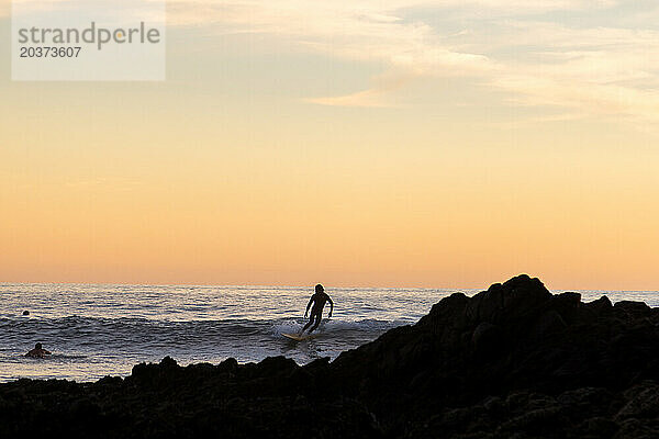 Eine Silhouette eines Surfers bei Sonnenuntergang.