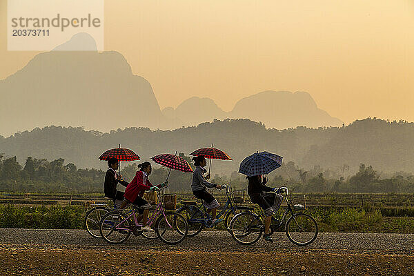 Eine Gruppe Mädchen fährt mit dem Fahrrad von der Schule und hält einen Regenschirm im Norden von Laos