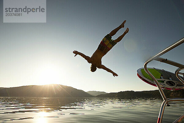 Ein sportlicher Mann springt bei Sonnenuntergang in Idaho von einem Wakeboard-Boot.