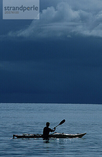 Silhouette eines Mannes  der mitten im Meer ein Kanu rudert.