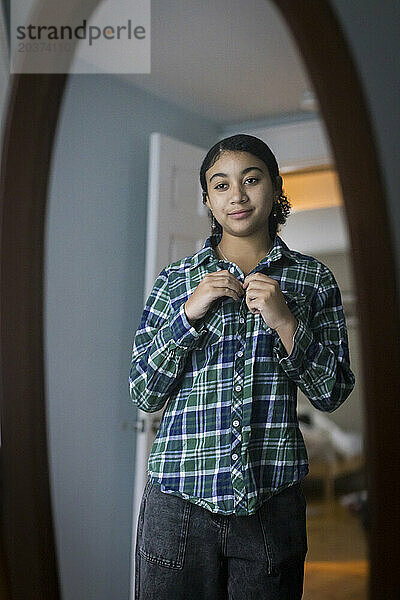 Biraciales Teenager-Mädchen schaut in den Spiegel  während es sein Hemd zuknöpft