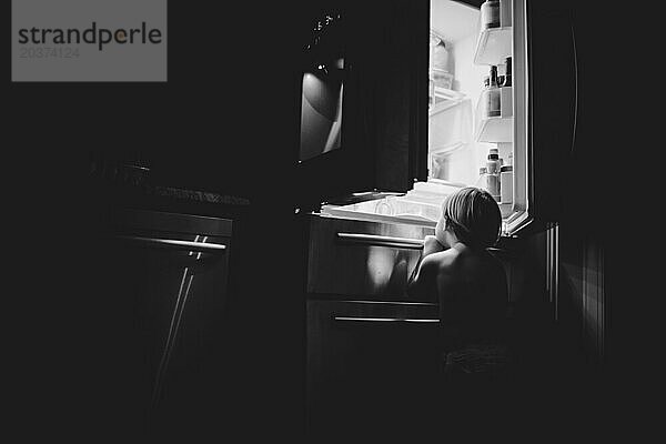 Ein Kind blickt in einem ruhigen Zuhause in den Glühen des Kühlschranks