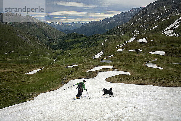 Ein Mann beim Skifahren mit seinem Hund in den französischen Alpen im Sommer am Col du St. Bernard  Savoie  Frankreich.