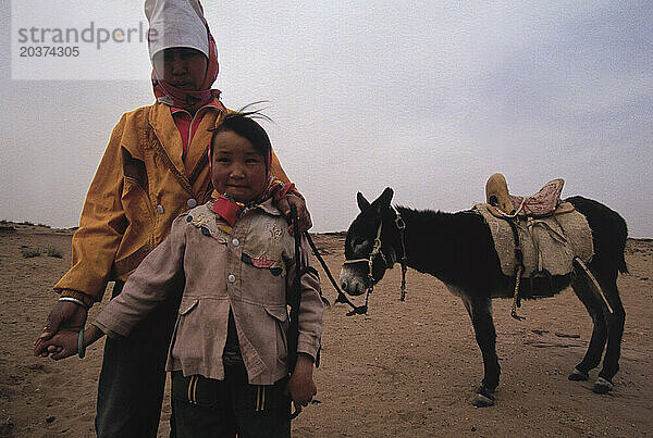 Mongolei - Mutter und Kind posieren vor einem gesattelten Esel