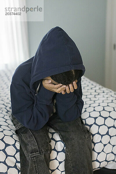 Ein gemischtrassiges Teenager-Mädchen sitzt auf dem Bett  den Kopf in die Hände gestützt  und sieht deprimiert aus