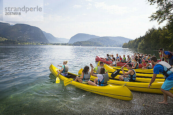 Junge Erwachsene einer Schulklasse betreten mit Kanus das Wasser des Bohinjer Sees in Slowenien